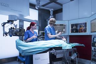 Medizinisches Personal in blauen Kitteln in einem Operationssaal mit zahlreichen technischen Gerätschaften