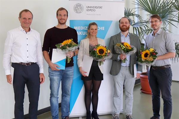 Fünf Menschen unterschiedlichen Alters posieren für ein Gruppenfoto. Vier Menschen haben Blumensträuße in der Hand.