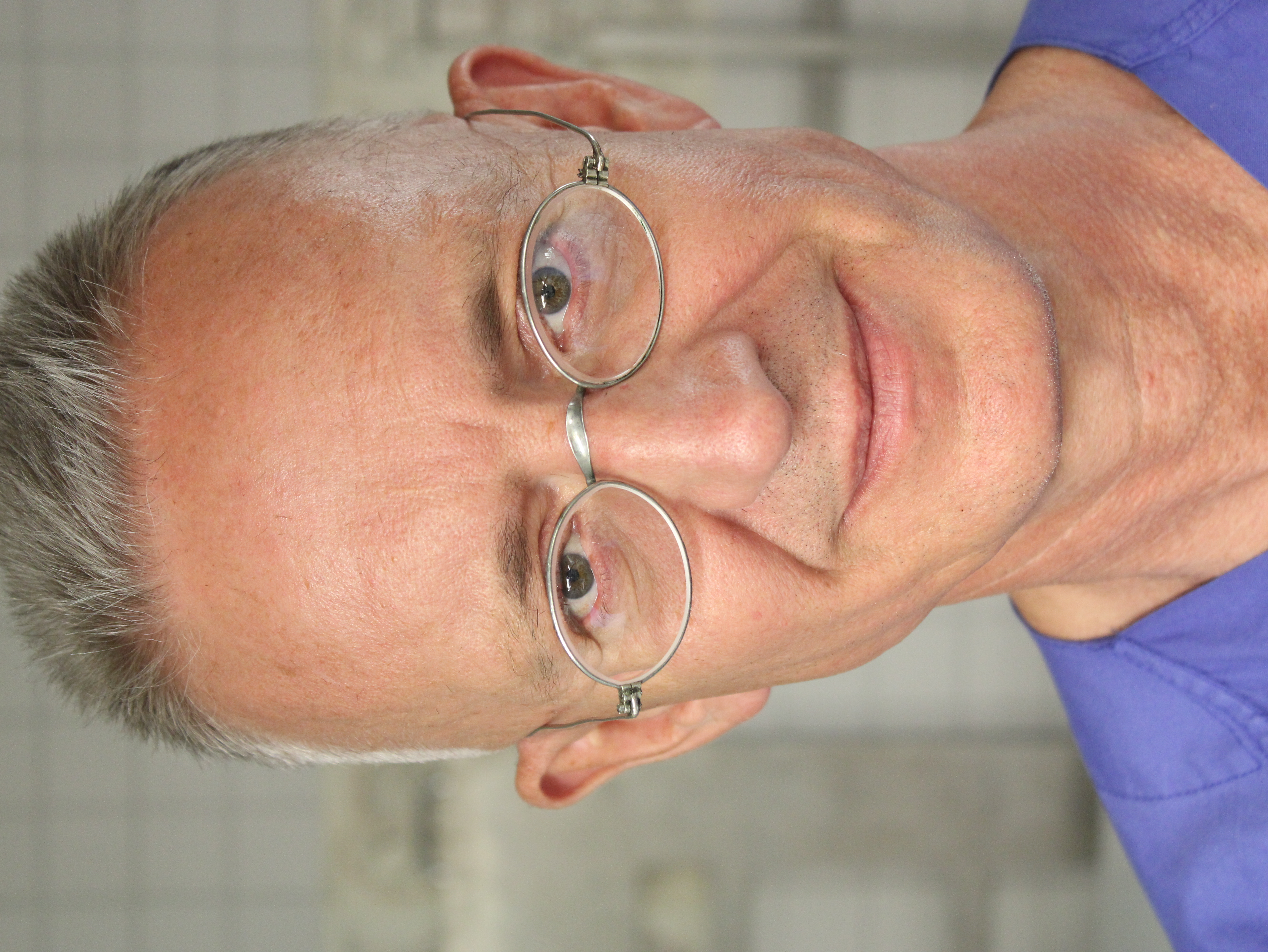 Bild eines Mannes mit runder Brille und kurzen, grauen Haaren.