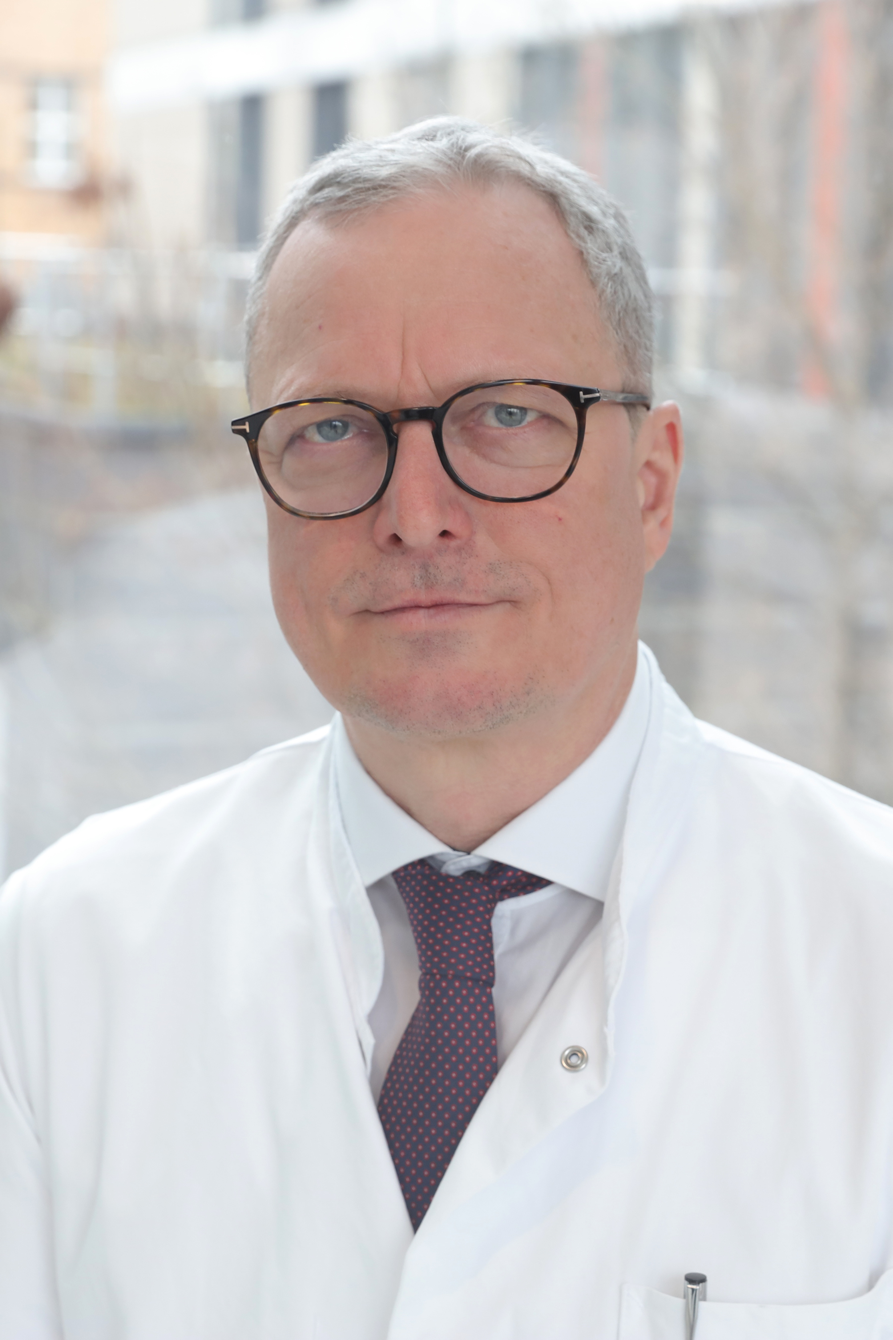 Image of a dark-haired, smiling middle-aged man. He wears dark-rimmed glasses and a white coat