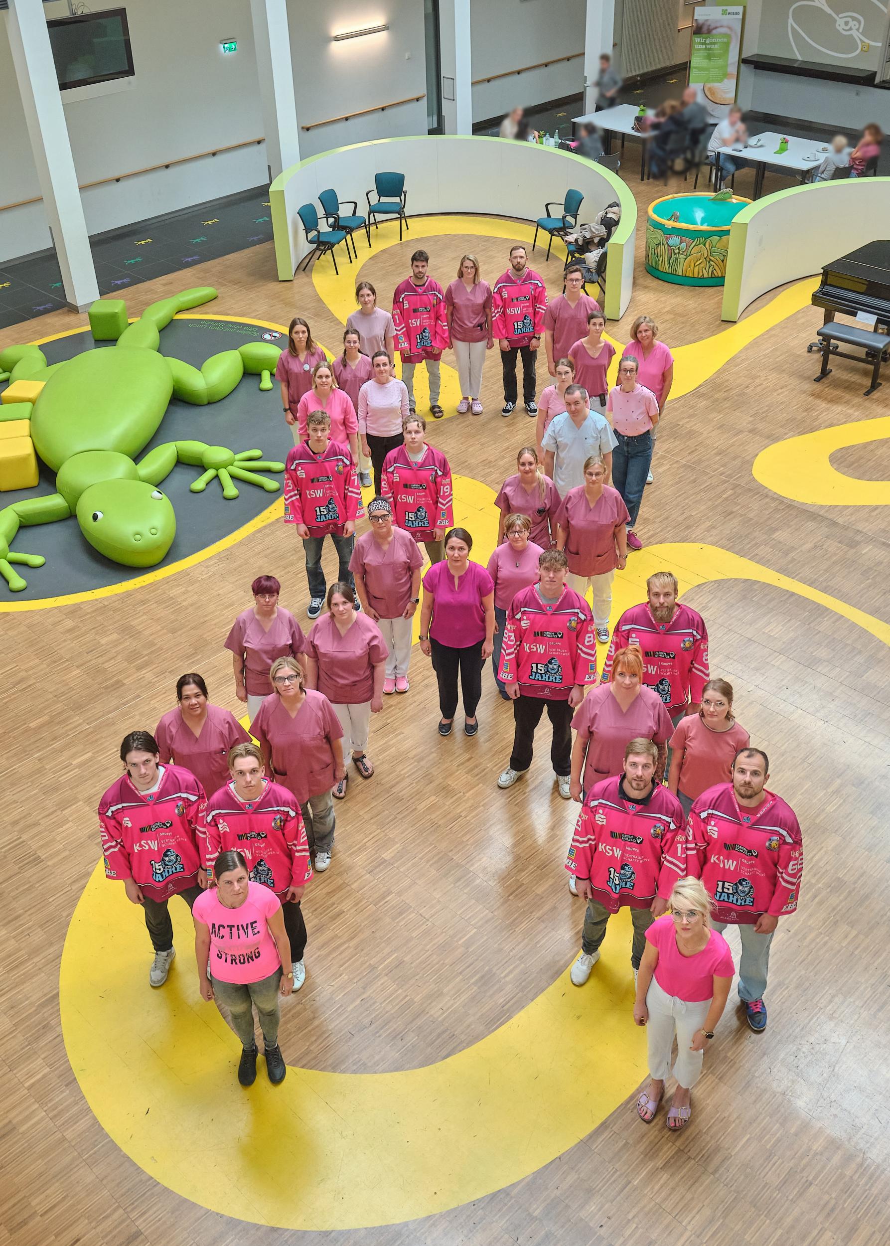 Gemeinsam gegen Brustkrebs: Mitarbeiter:innen des UKL-Brustzentrums und Spieler der KSW IceFighters Leipzig bilden eine symbolische rosa Schleife, um für das Anliegen der Aktion zu werben.