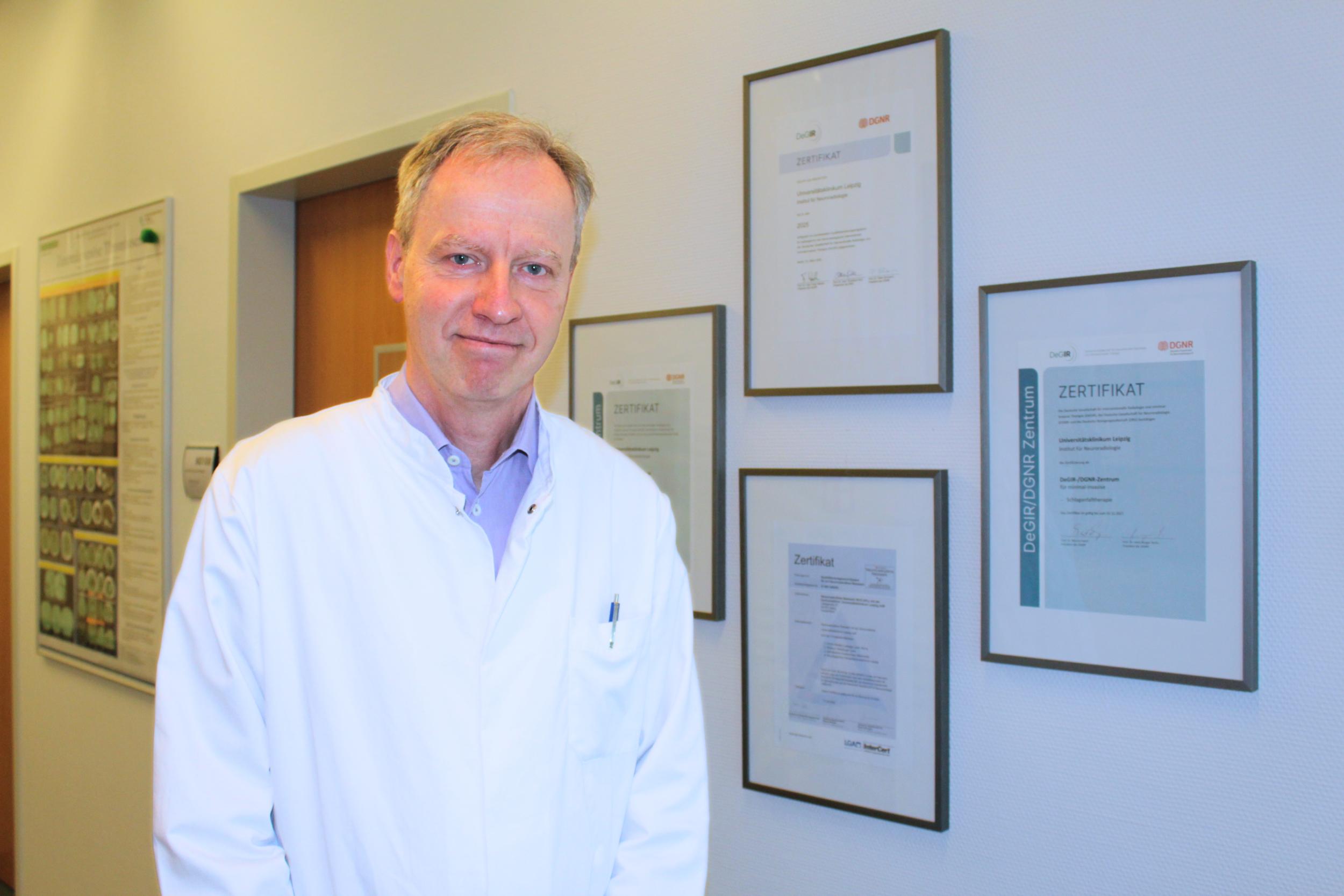 Prof. Dr. Karl-Titus Hoffmann vor den zahlreichen Zertifikaten, die das  Institut für Neuroradiologie am UKL bereits erhalten hat.