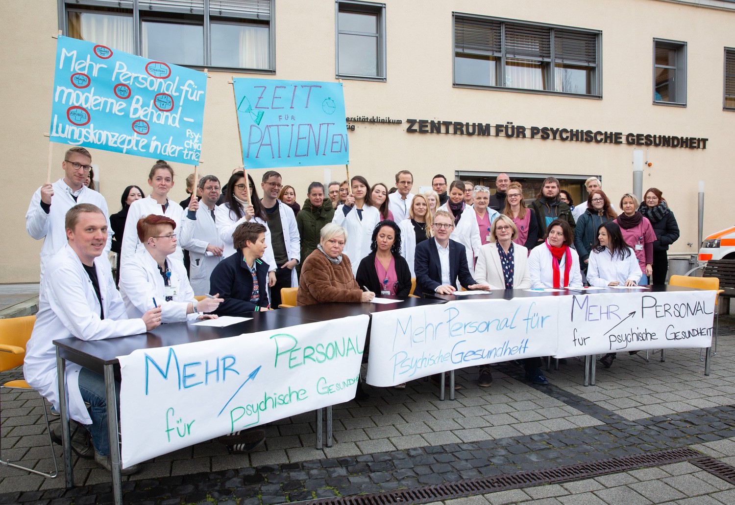 Draußen statt drinnen: Aus Protest gegen die neue Richtlinie zur Personalausstattung haben Mitarbeiter der UKL-Kliniken für Psychiatrie und für Psychosomatik ihre Teamsitzung auf die Straße verlegt. Mit dabei die Klinikdirektoren Prof. Anette Kersting (sitzend, 3.v.r.) und Prof. Georg Schomerus (sitzend, 4.v.r.).