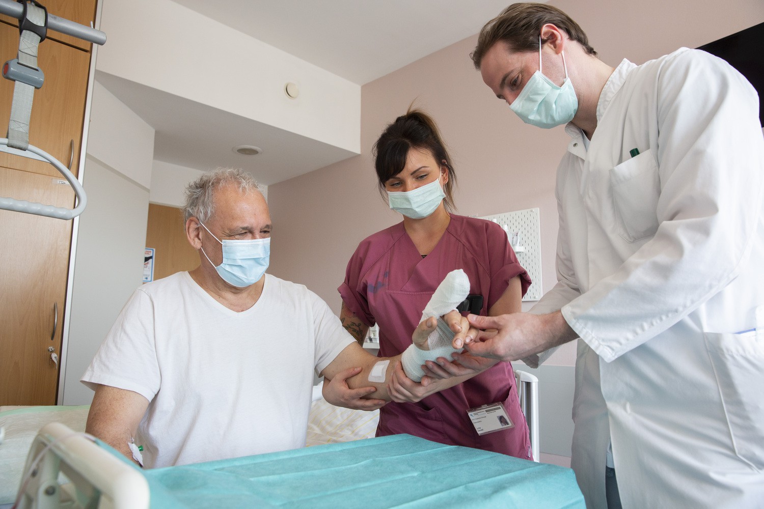 Constantin Weil von der Ahe (re.), behandelnder Arzt der Klinik und Poliklinik für Orthopädie, Unfallchirurgie und Plastische Chirurgie, und Schwester Julia Seidel (Mi.), bei einer Kontrolluntersuchung des replantierten Fingers. Der 63-jährige Patient (li.) hatte sich den Zeigefinger der linken Hand beim Holzhacken fast komplett abgetrennt.