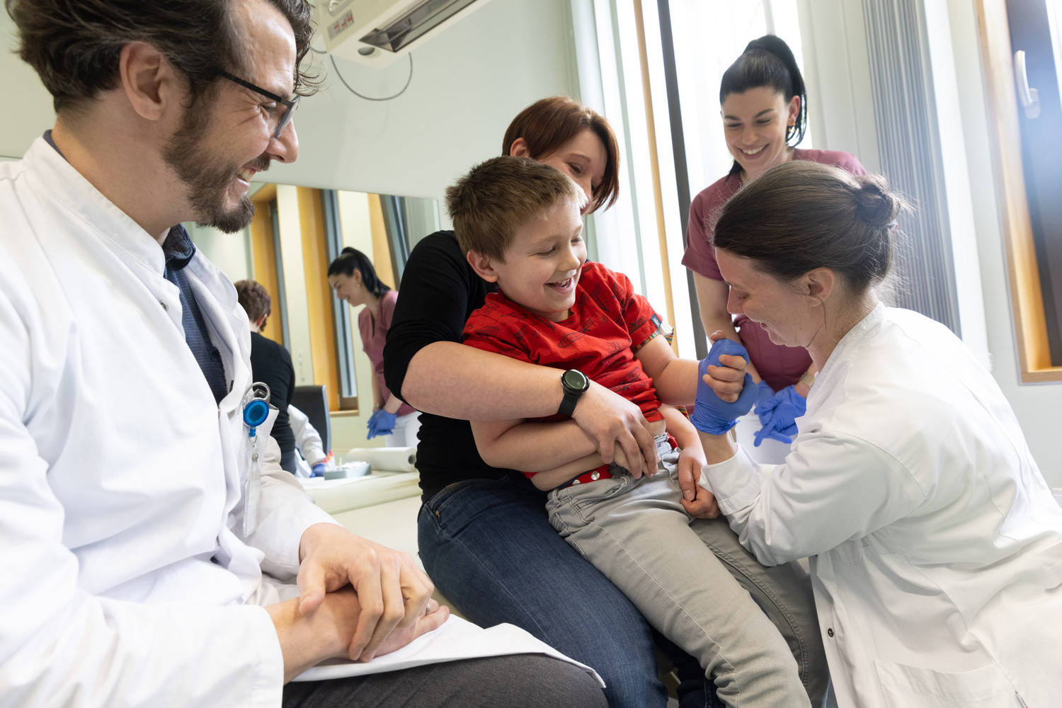 Felix gewinnt das Armdrücken gegen Dr. Olga Hempel (re.), Assistenzärztin im Bereich von Prof. Klemann (li.), der genau wie Schwester Nadine Steigert (2.v.r.) mitfiebert. Gewünschter Nebeneffekt der Aktion: Felix muss Blut abgenommen werden und auf diese Weise gelingt es Dr. Hempel spielerisch, die Venen für eine mögliche Einstichstelle besser hervortreten zu lassen.